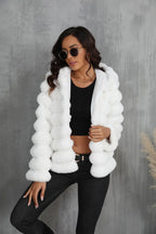 Woman wearing a white hooded faux fur jacket with horizontal stripe pattern, cropped silhouette, and zipper closure.