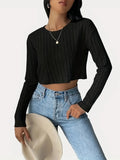 Woman wearing a black ribbed cropped long-sleeve shirt and light wash jeans, holding a hat, front view