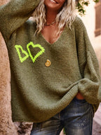 Front view of a woman in an olive green V-neck knit sweater with neon yellow heart embroidery, showing the relaxed fit and dropped shoulders.