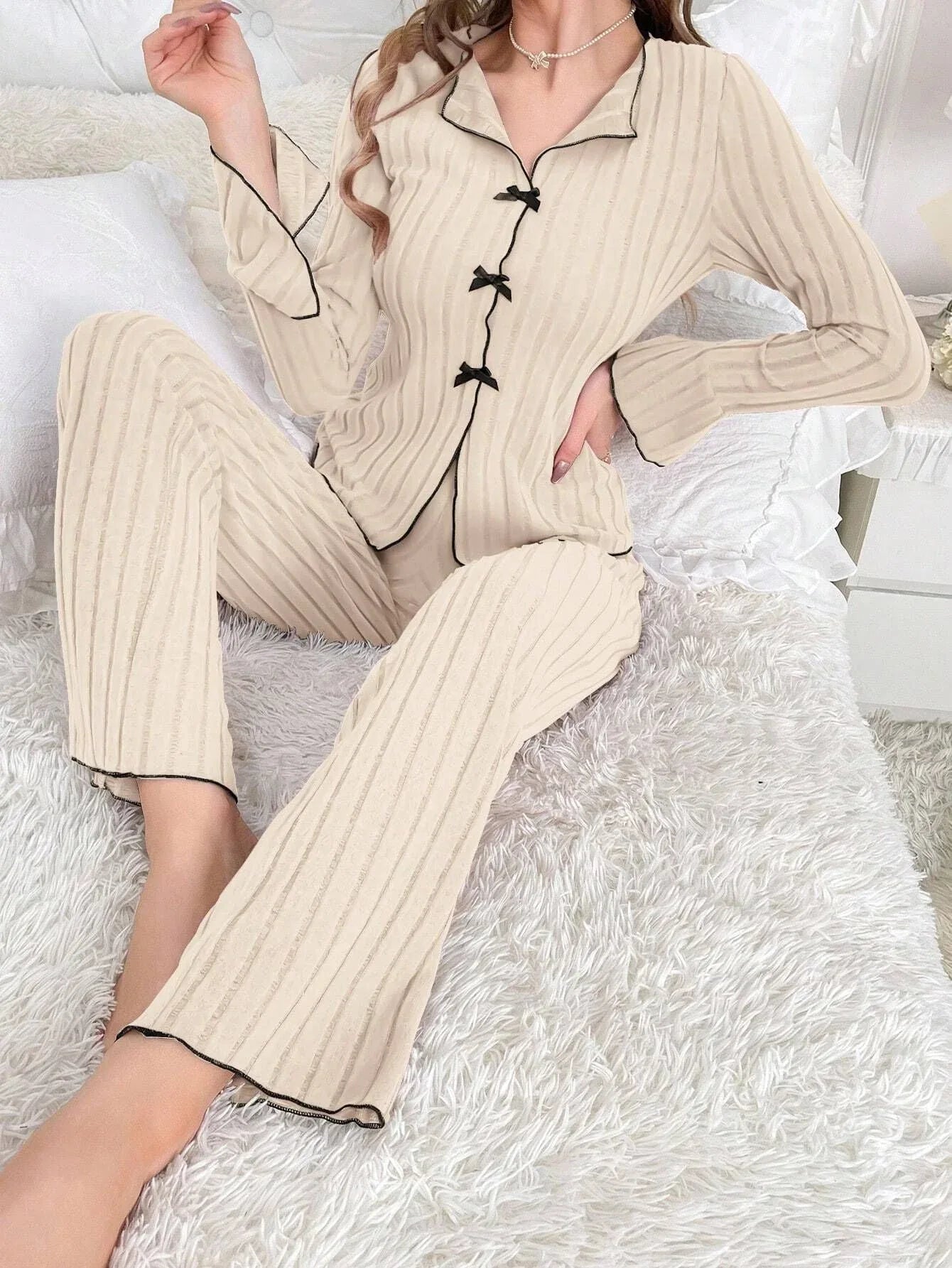 Woman sitting on a bed wearing a cherry print pajama set and holding a mug.