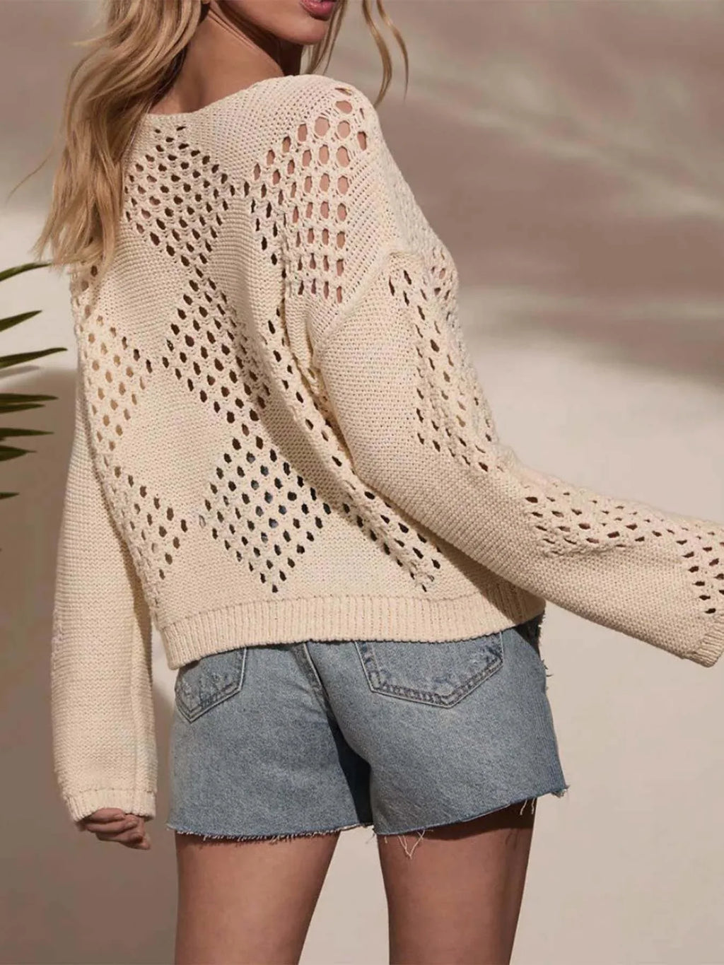 Back view of a woman in a cream open-knit sweater with diamond stitch detail.