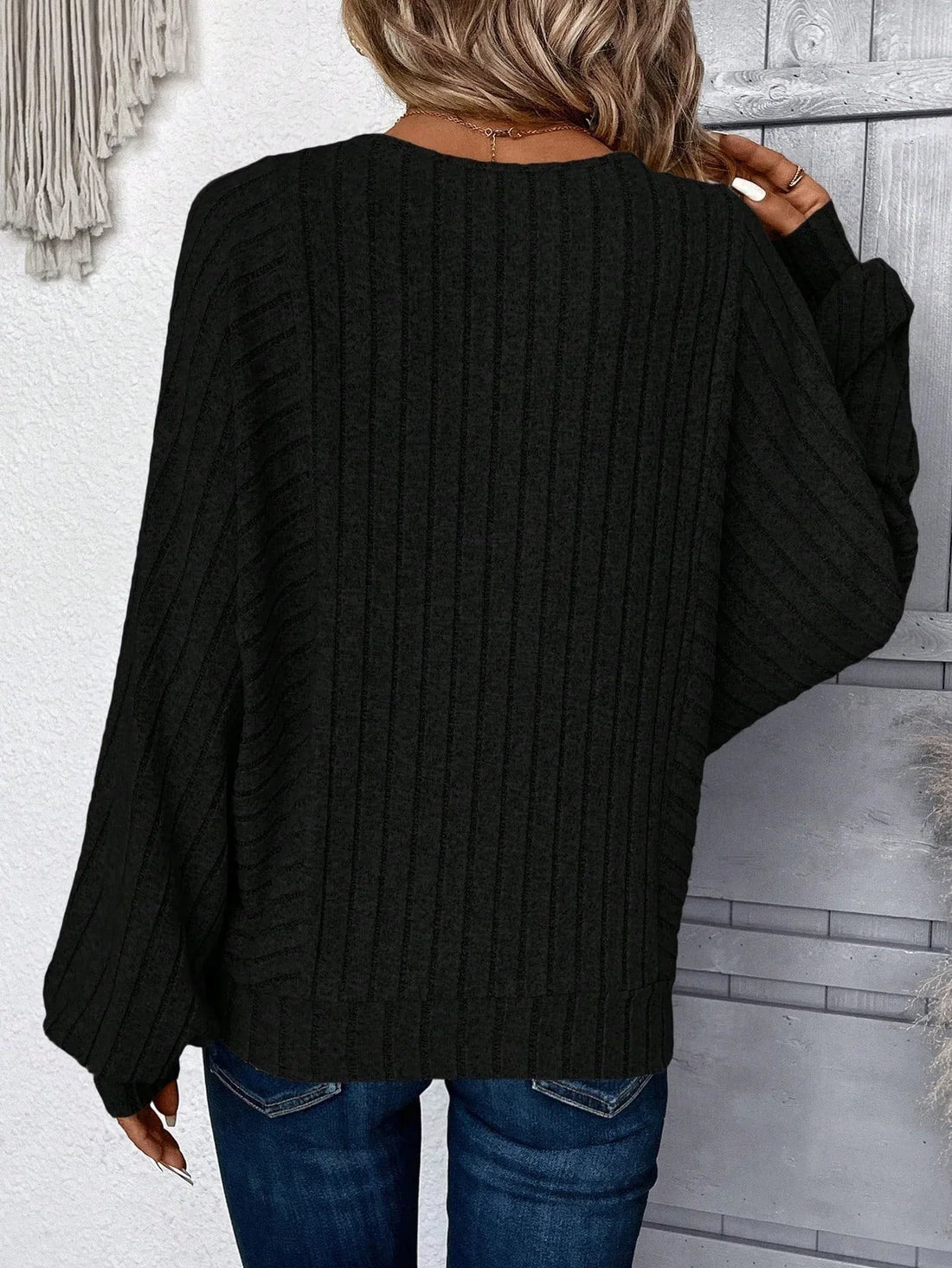 Woman wearing a black ribbed knit sweater with wide sleeves and round neckline, paired with blue jeans.