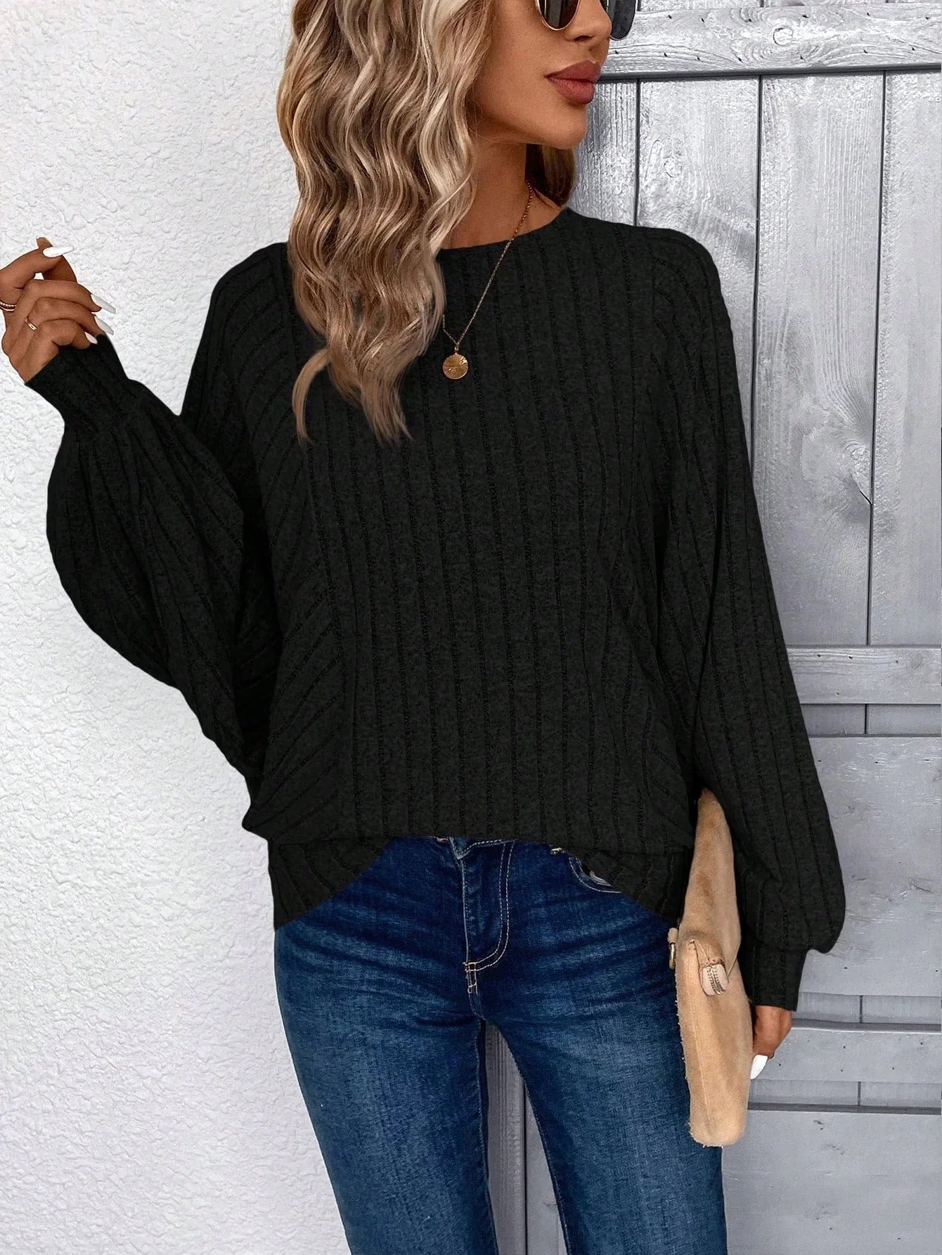 Woman posing in a black ribbed knit sweater and blue jeans.