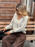 Woman sitting on a bench wearing a cream argyle knit cardigan and brown pants.