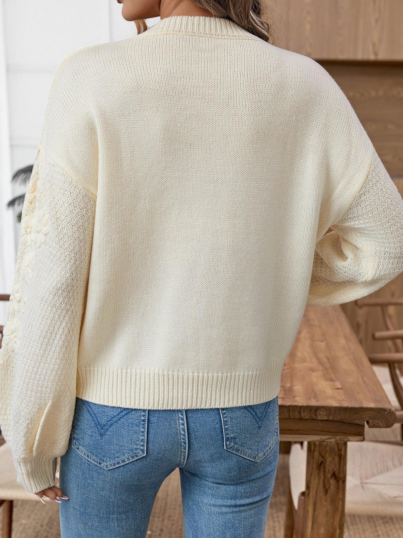 Back view of a woman in a cream knit sweater with floral embroidery on the sleeves.