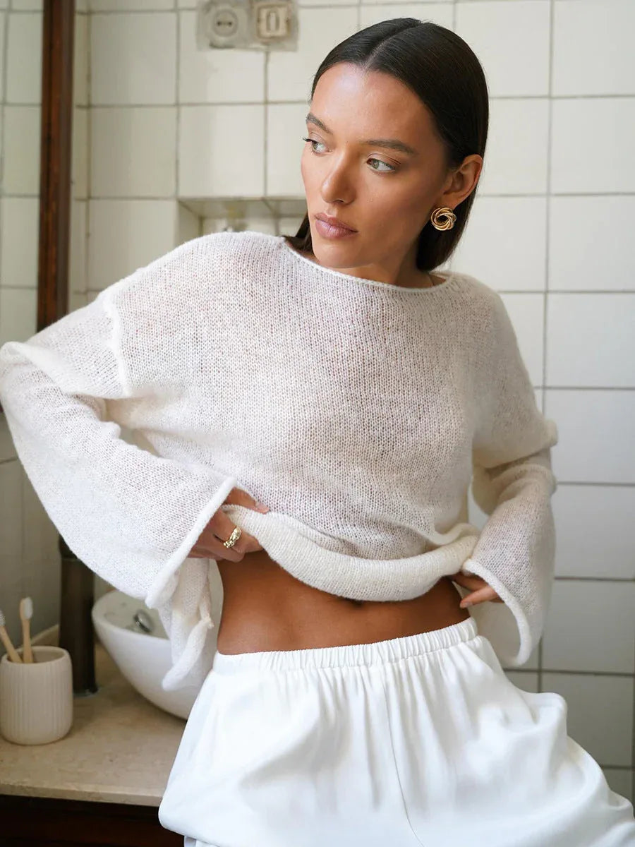Woman in a white sheer knit sweater showing the waistband of her white pants.