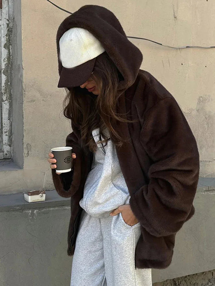 Woman wearing a brown faux fur hooded jacket and a baseball cap.