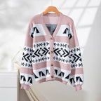 Pink, white, and black geometric pattern knit cardigan with V-neck and button-up closure hanging on a wooden hanger.