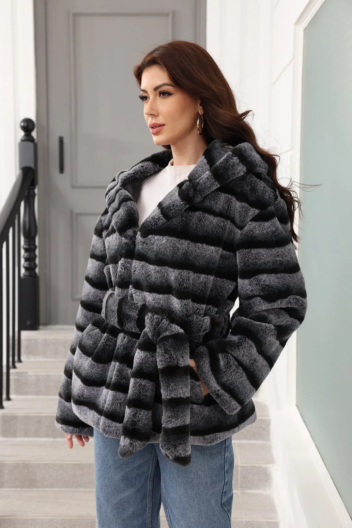 Side view of a woman in a hooded, belted, grey and black striped faux fur jacket.