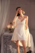 Woman wearing a cream slip dress and matching robe, standing by a table with candles.