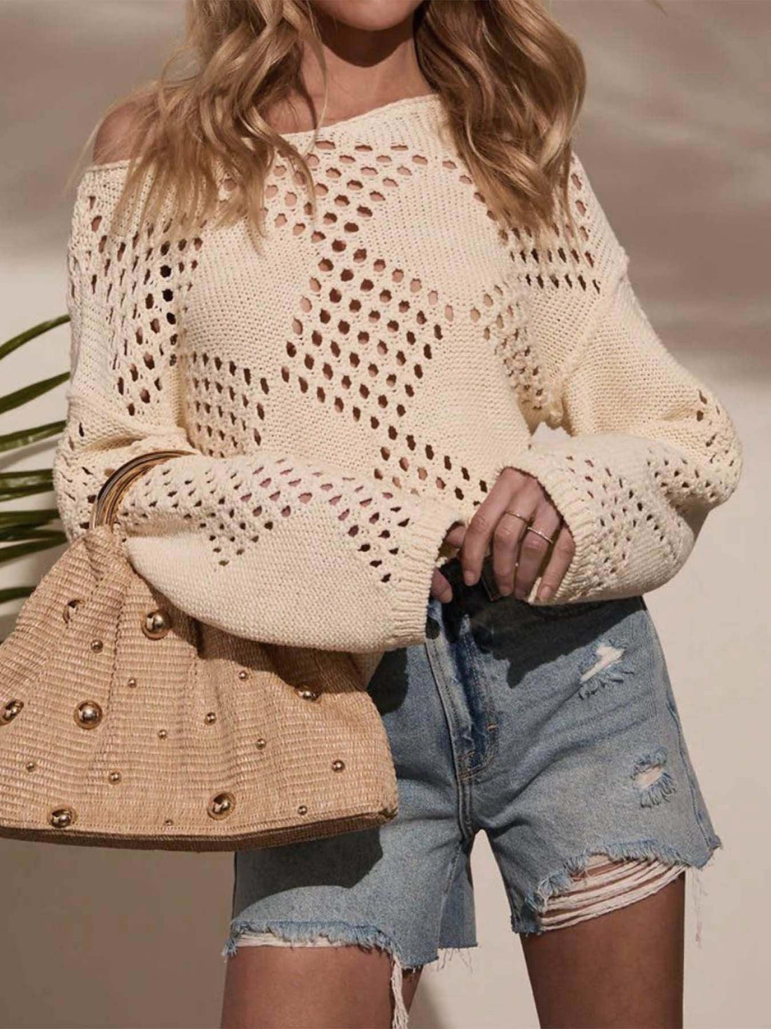 Woman wearing a cream open-knit sweater with diamond stitch detail and light wash denim shorts.