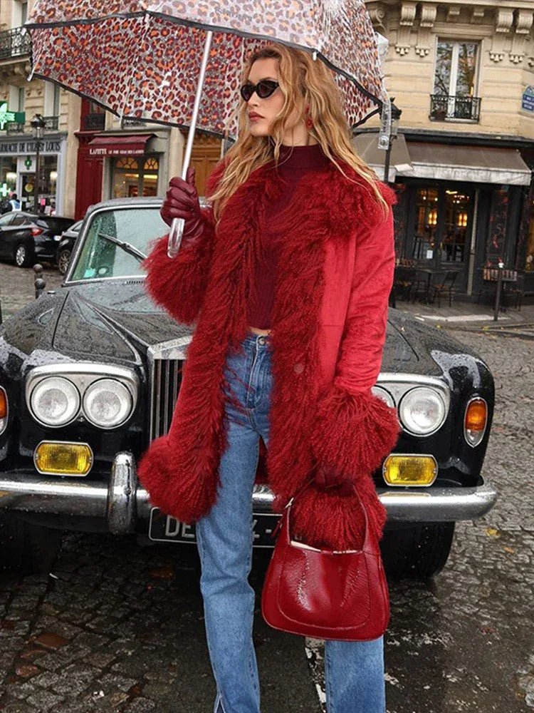 Woman standing in front of a vintage car, wearing a red faux fur trimmed coat, burgundy turtleneck, blue jeans, and holding a leopard print umbrella.