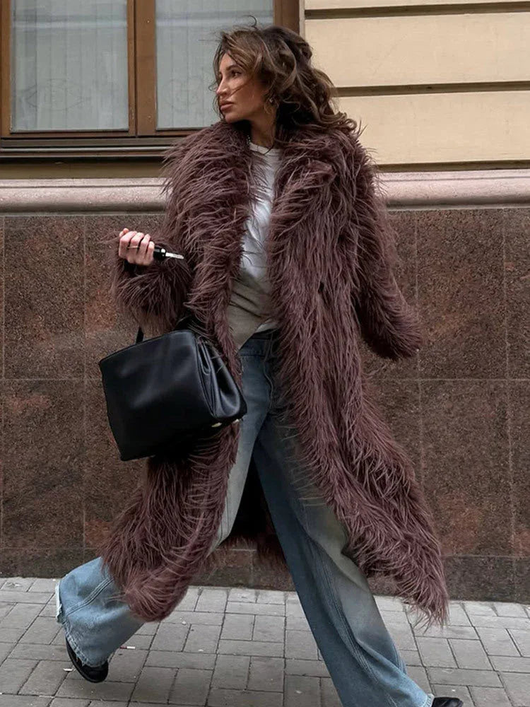 Woman wearing a long brown shaggy faux fur coat and blue jeans, holding a black handbag. Main image