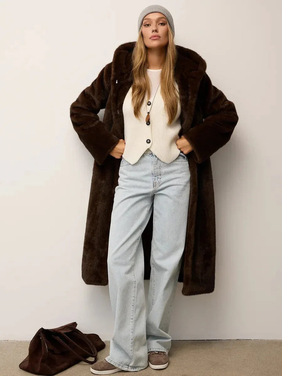 Full body shot of a woman in a brown faux fur hooded coat, white vest, and light wash jeans.