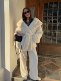 Model posing in a white oversized faux fur coat with a belt and matching white pants.