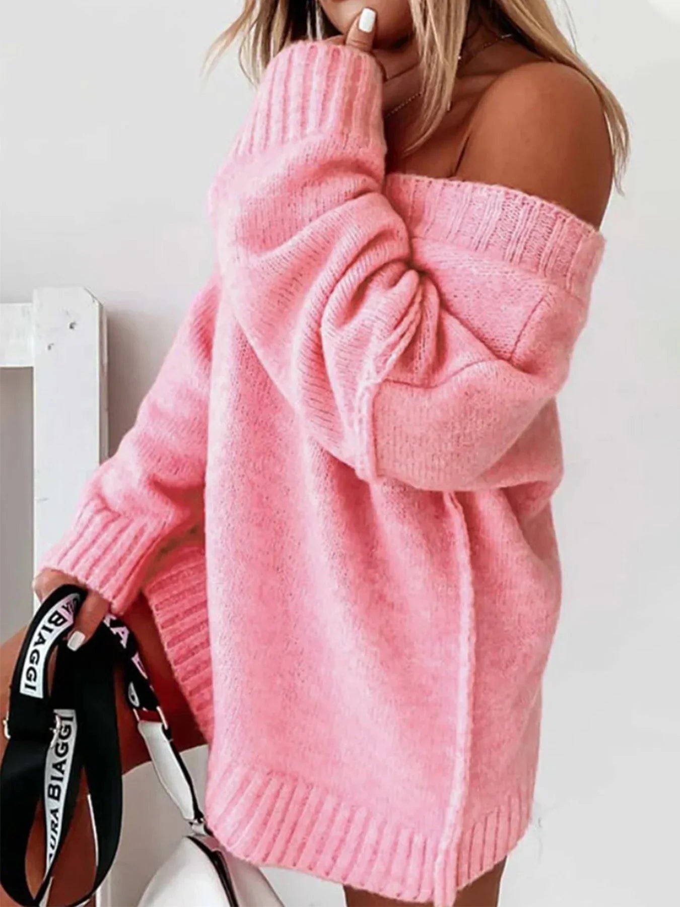 Woman in a pink oversized knit sweater with sleeves pushed up, holding a black and white bag.