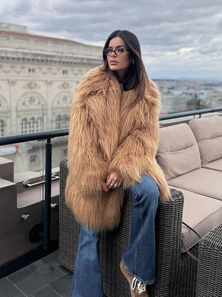 Woman wearing a tan shaggy faux fur coat and blue jeans sitting on a balcony couch Main image