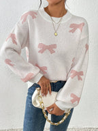 Woman in a white knit sweater with a pink bow print, holding a white clutch bag.