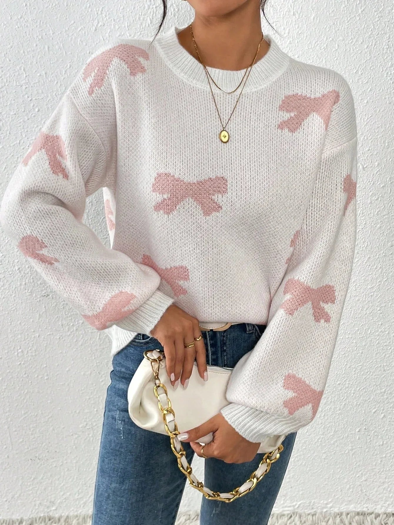 Woman in a white knit sweater with a pink bow print, holding a white clutch bag.