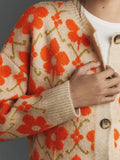 Close-up of the sleeve and front of a beige cardigan with an orange floral print.