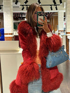 Close-up of a woman in a red faux fur trimmed coat, holding a blue handbag and a phone.