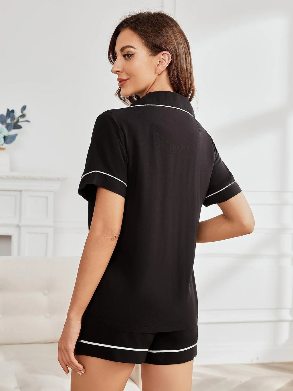 Rear view of a woman wearing a black short-sleeve pajama top with white piping.