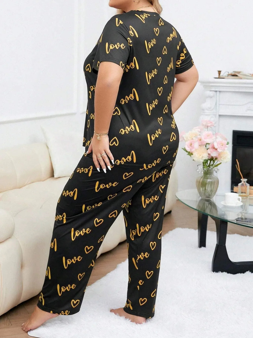 Woman wearing a black short-sleeve pajama top and pants with a gold heart and 'love' graphic print, viewed from the side.