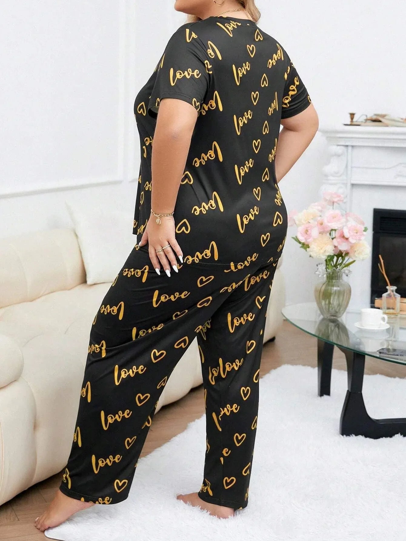 Woman wearing a black short-sleeve pajama top and pants with a gold heart and 'love' graphic print, viewed from the side.
