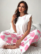 Woman wearing white top with ruffled sleeves and pink heart print pajamas sitting on a bed