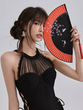 Close-up of a woman wearing a black one-piece swimsuit with a sheer mesh halter neckline, holding a red and black fan.