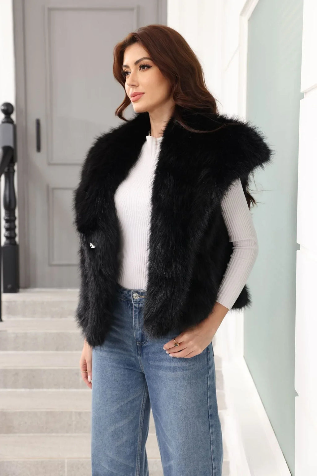 Woman wearing a black faux fur vest and blue jeans, posing with hands on hips.
