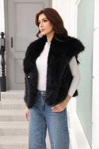 Woman wearing a black faux fur vest and blue jeans, posing with hands on hips.