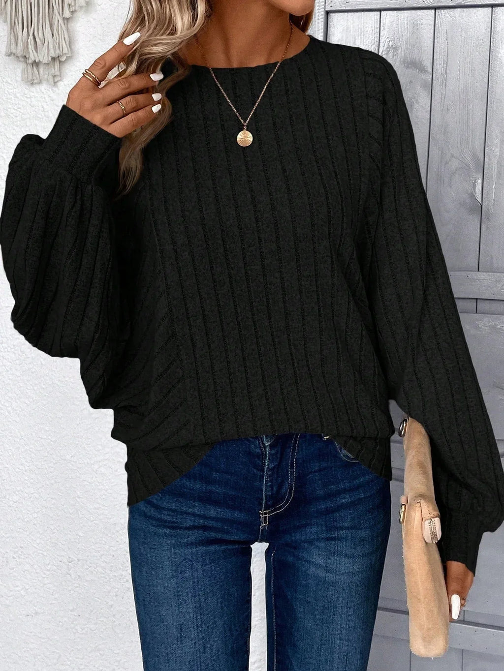 Front view of a woman in a black ribbed knit sweater, holding a clutch.