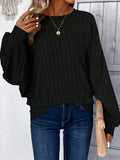 Front view of a woman in a black ribbed knit sweater, holding a clutch.