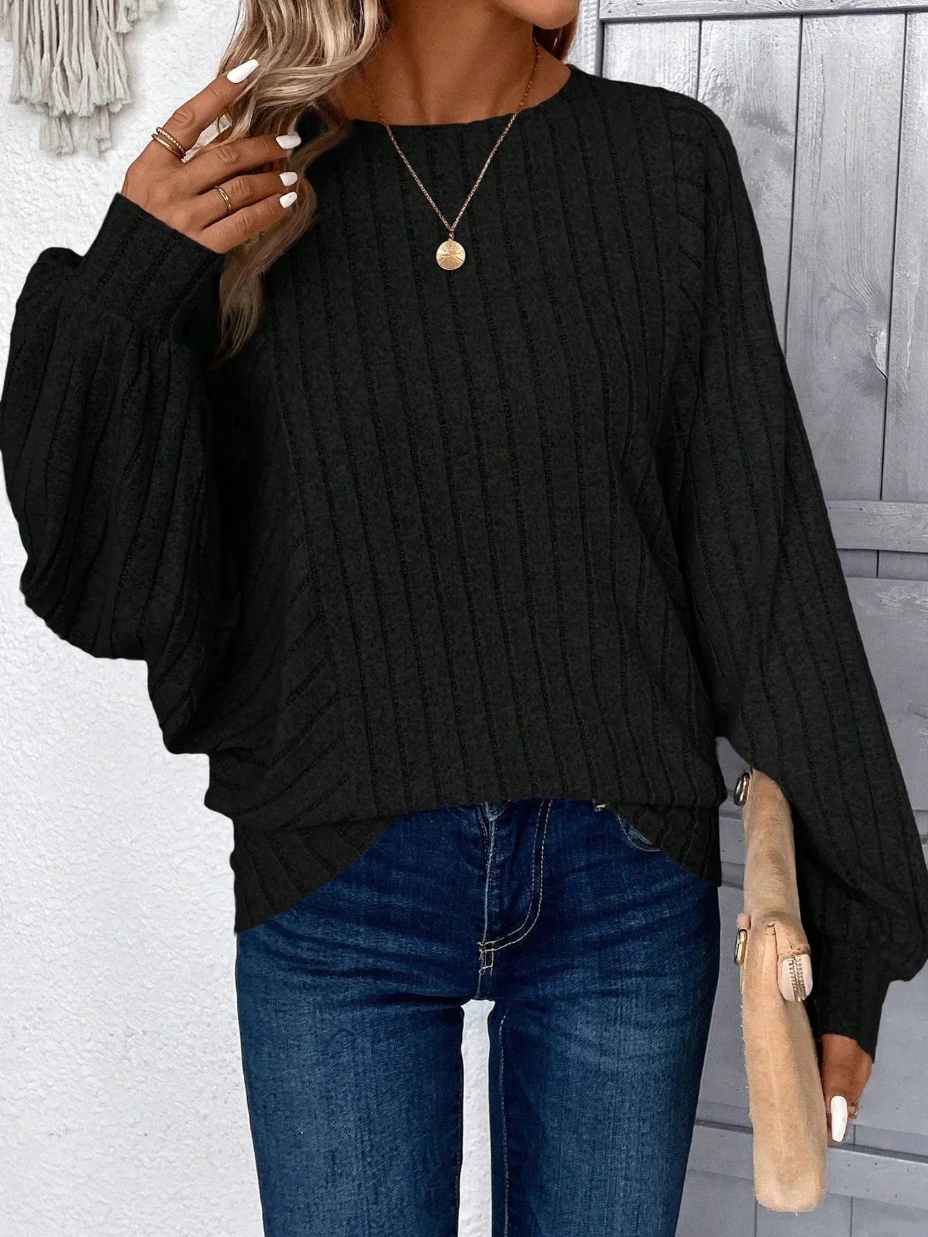 Front view of a woman in a black ribbed knit sweater, holding a clutch.
