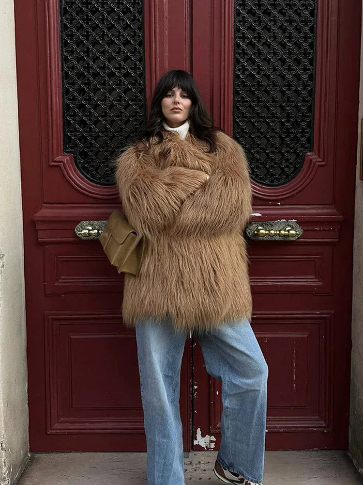 Full body shot of a woman wearing a tan shaggy faux fur coat, white turtleneck, and blue jeans