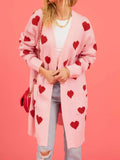 Woman wearing a pink longline knit cardigan with a red heart pattern and two front pockets.