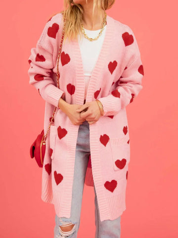 Woman wearing a pink longline knit cardigan with a red heart pattern and two front pockets.
