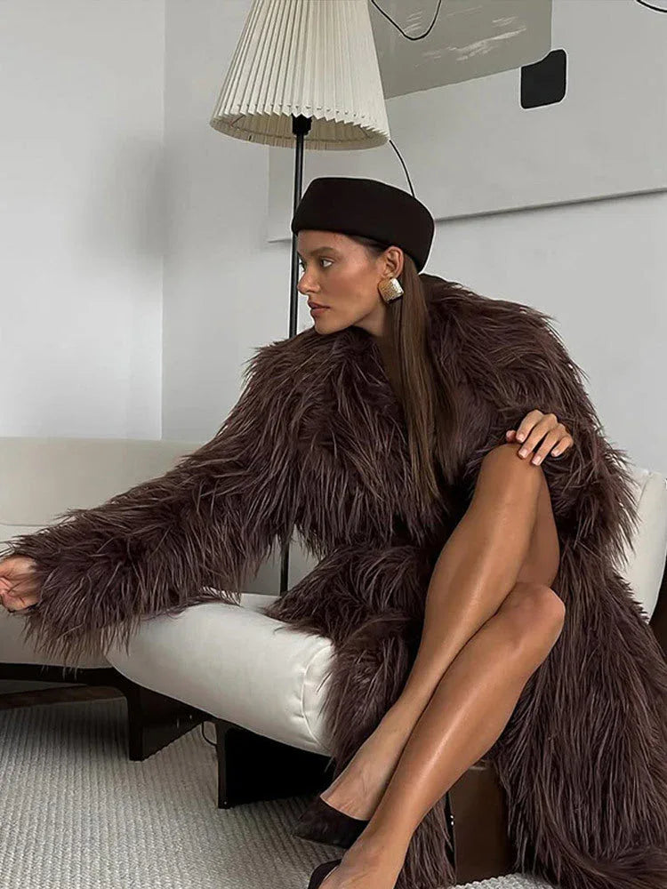 Woman sitting on a white sofa wearing a long brown shaggy faux fur coat and a brown beret.