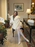 Woman sitting in a chair wearing a white faux fur robe-style coat indoors.