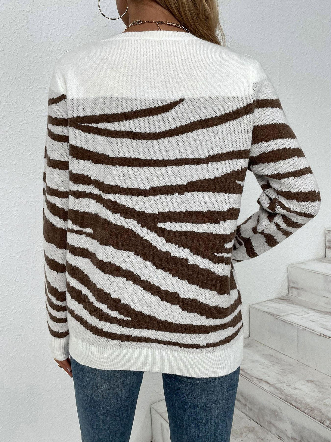 Woman wearing a white and brown zebra print crew neck sweater with gold shoulder buttons