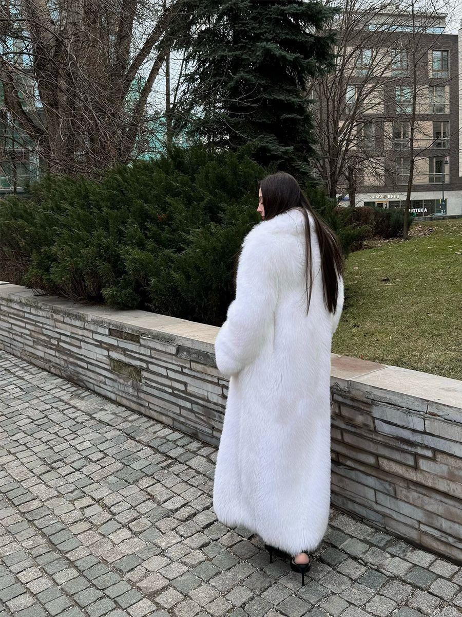Rear view of a woman in a long white faux fur coat walking outdoors.