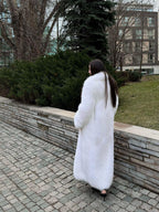 Rear view of a woman in a long white faux fur coat walking outdoors.
