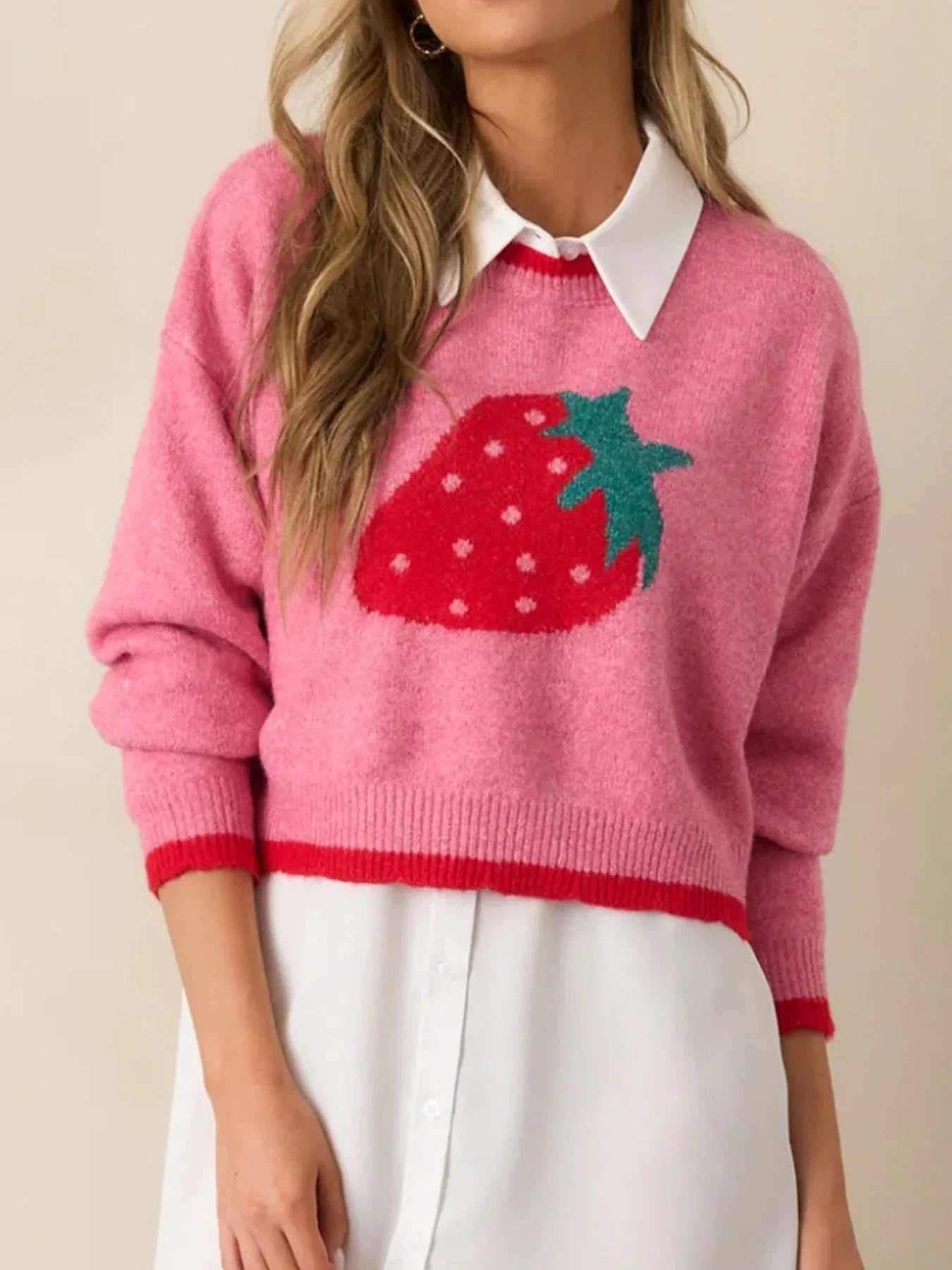 Woman wearing a pink cropped knit sweater with a strawberry graphic, showing the neckline and collar of an underlayer.