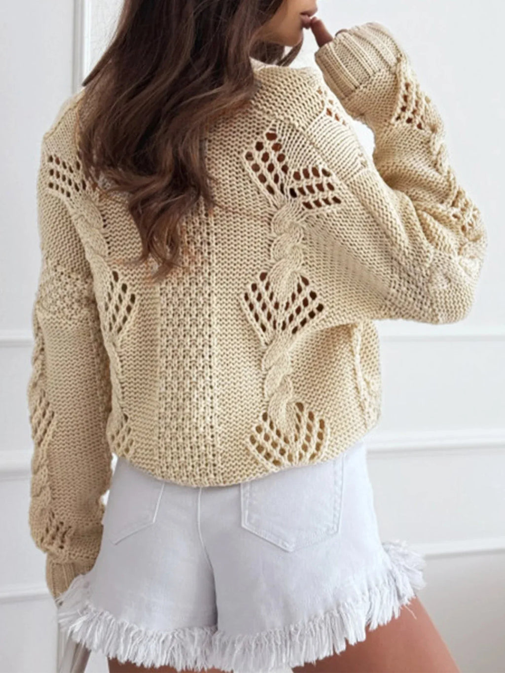 Back view of a beige cropped knit cardigan showing the open knit pattern.
