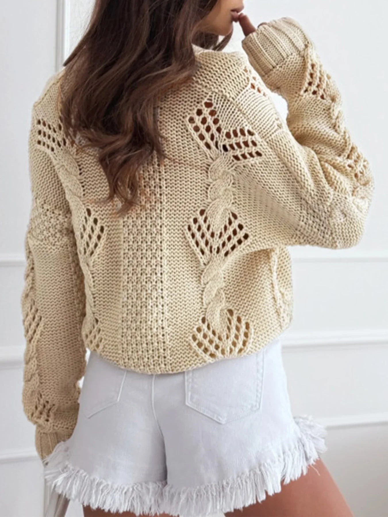 Back view of a beige cropped knit cardigan showing the open knit pattern.
