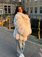 Woman in a white faux fur coat with a wide collar, standing on a bridge.
