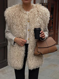 Close-up of a woman wearing a beige shaggy faux fur vest over a light grey sweater with gold buttons.