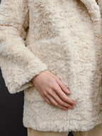 Detail shot of the cream faux fur coat sleeve and pocket.