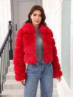 Woman wearing a red faux fur cropped jacket with a collared neckline and zipper closure, paired with a grey turtleneck and blue denim jeans.